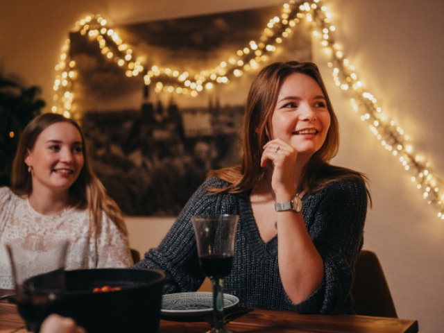 Zwei junge Frauen sitzen an einem gedeckten Tisch und schauen lächelnd aus dem Bild heraus