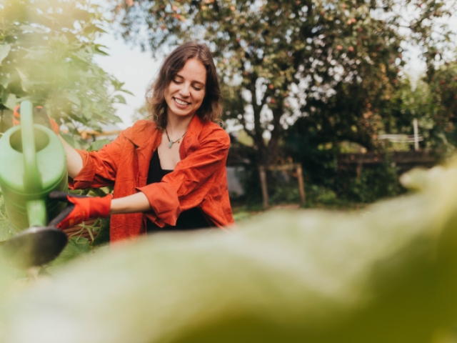 Eine junge Frau gießt lächelnd Blumen mit einer Gießkanne